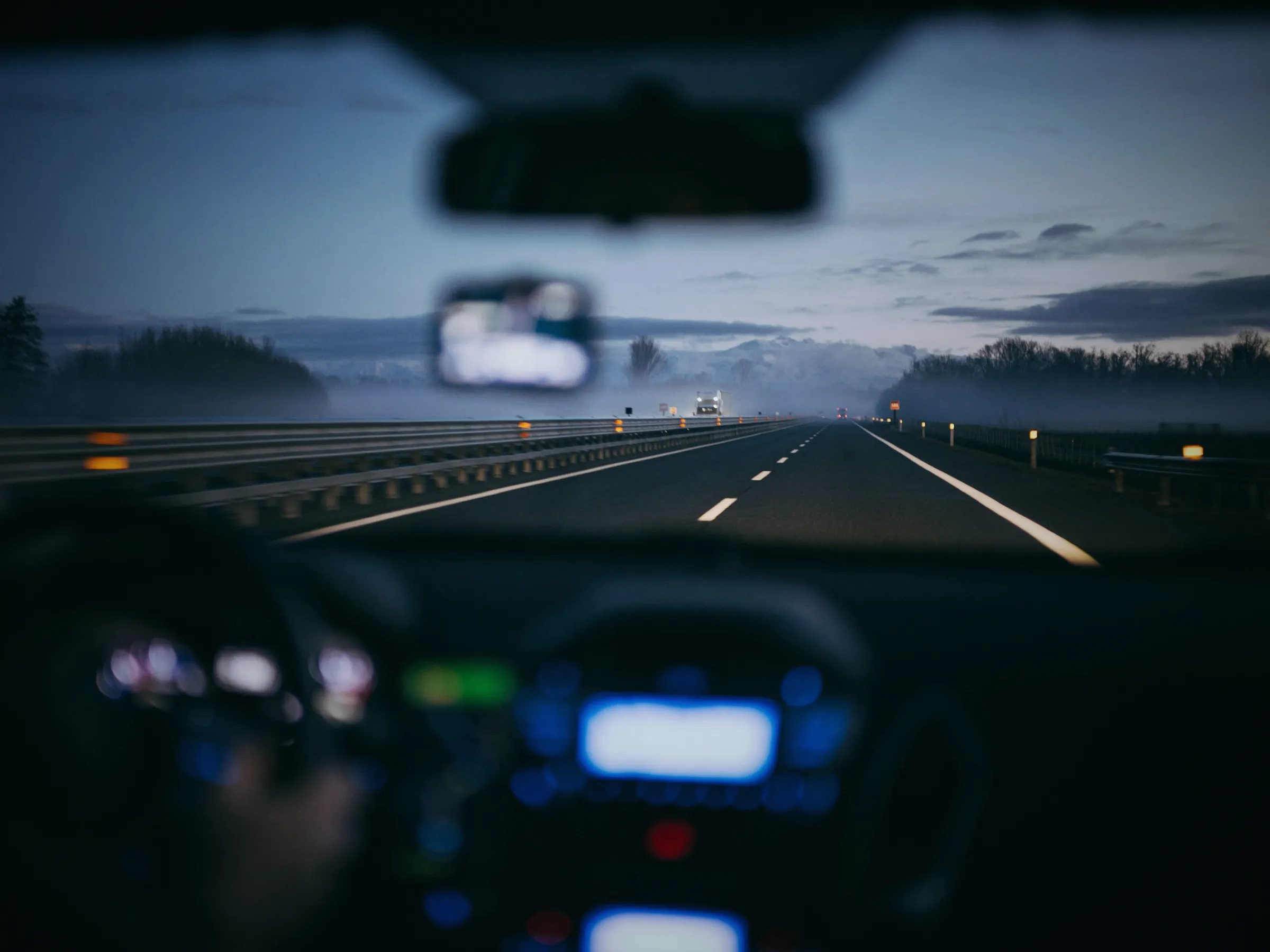 Dusk highway seen through a car windshield, the instrument lights glowing below