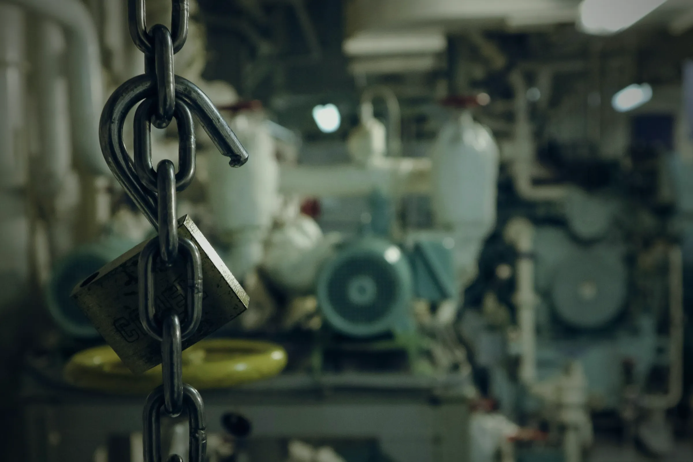 A padlocked chain hanging in a ship's engine room, machinery behind it