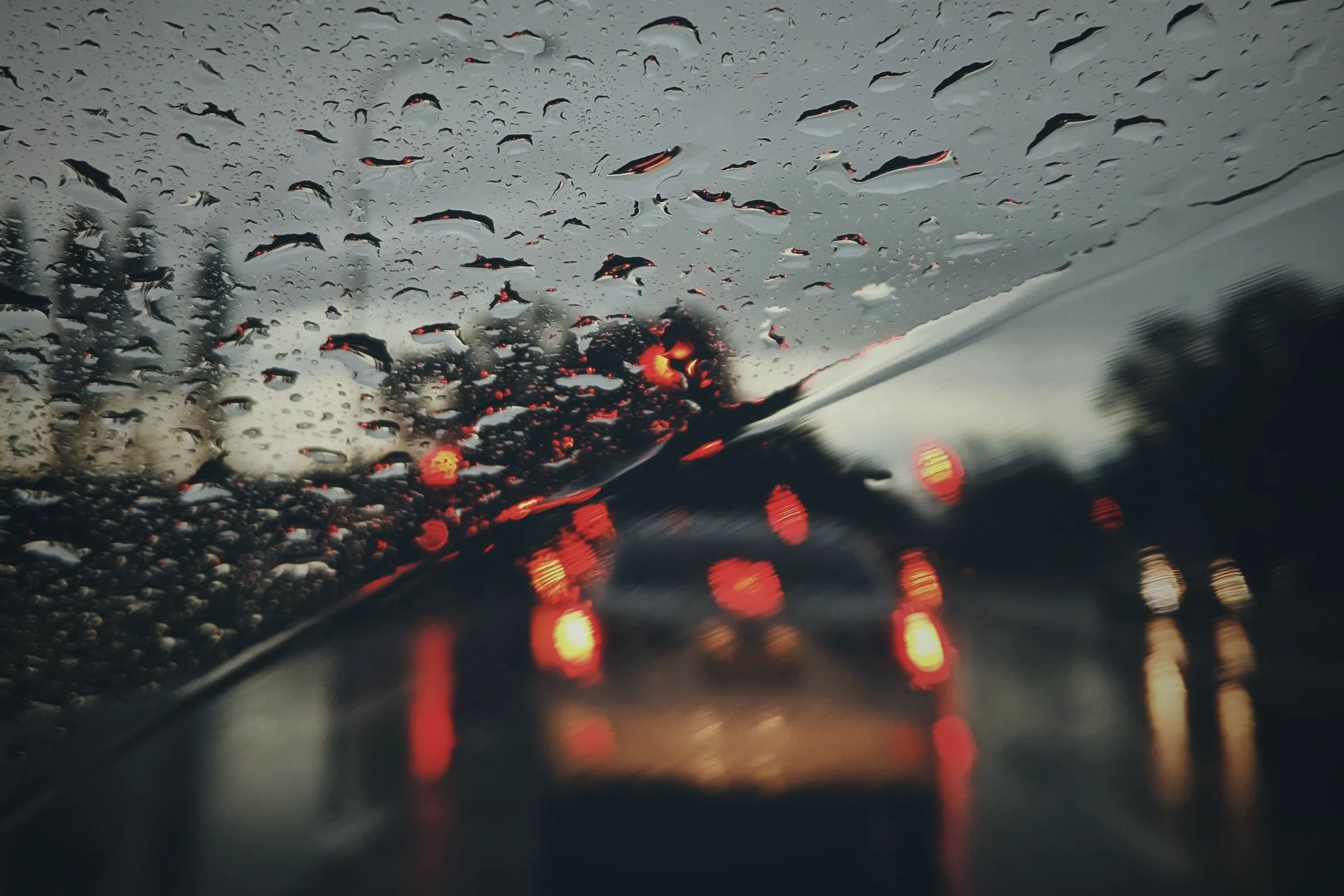 Red brake lights of traffic ahead, blurred through rain on a windshield